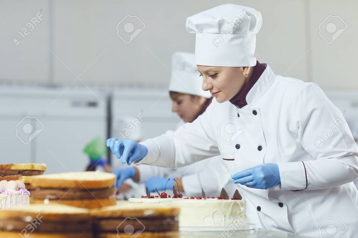 126666660-pastelero-de-mujer-con-pastel-de-pasteleria-en-la-mano-sonriendo-en-la-panaderia.jpg